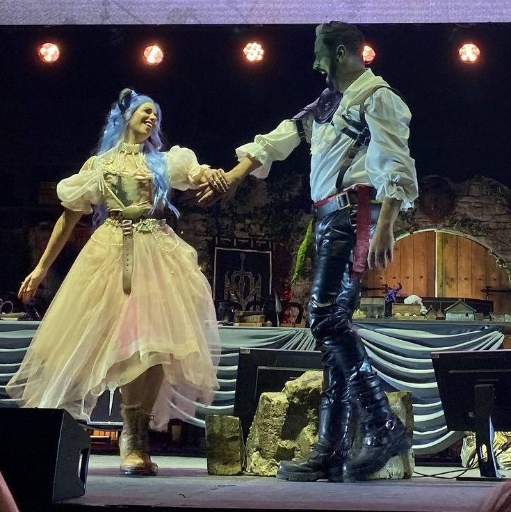 a man and woman dressed in pirate costumes dancing on stage with their hands clasped together