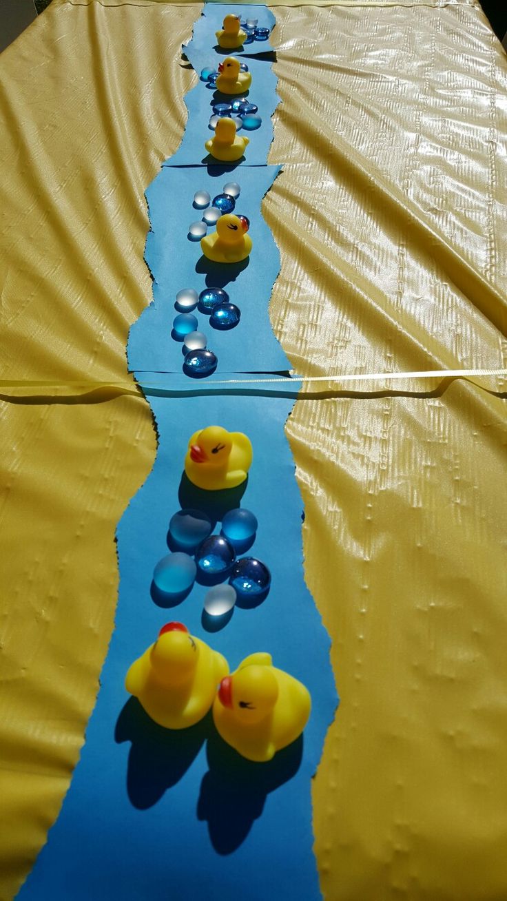 several rubber ducks lined up on a yellow and blue table cloth with water in between them