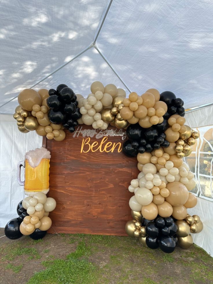 an arch made out of balloons with a beer mug and sign on the side under a tent