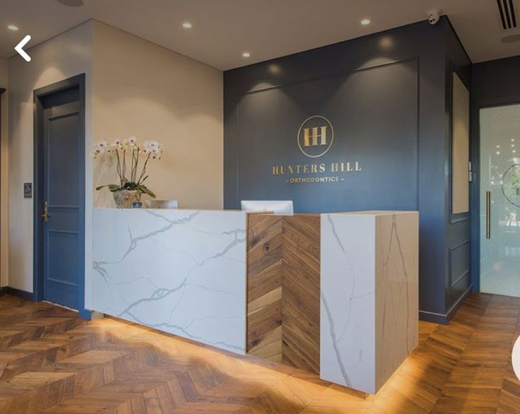 the front desk of a hotel lobby with wood flooring and blue walls, along with white marble counter tops