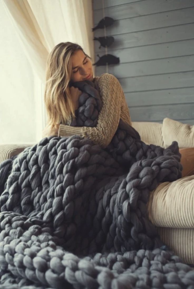 a woman laying on top of a bed covered in a giant chunk knit blanket next to a window