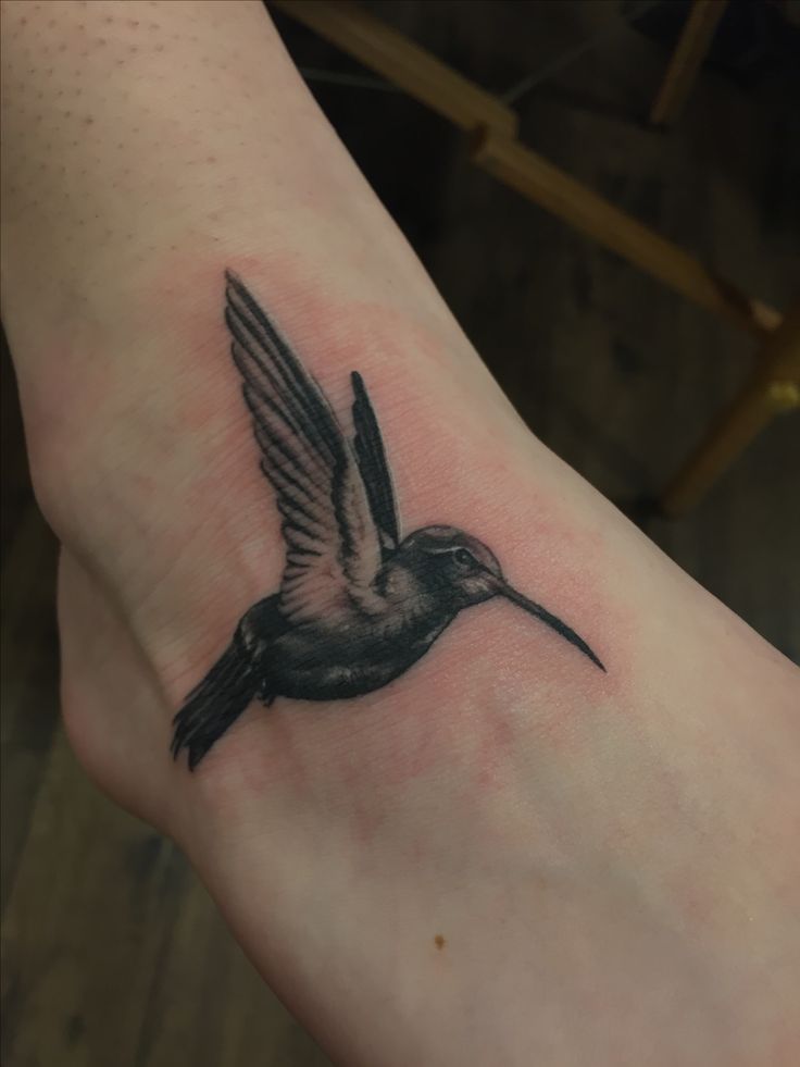 a small black and white hummingbird tattoo on the foot