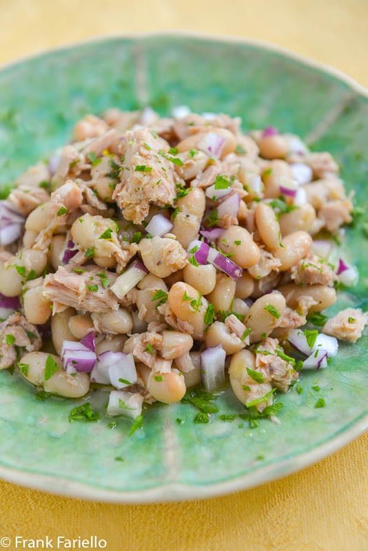 a green plate filled with beans and meat on top of a table next to a yellow cloth