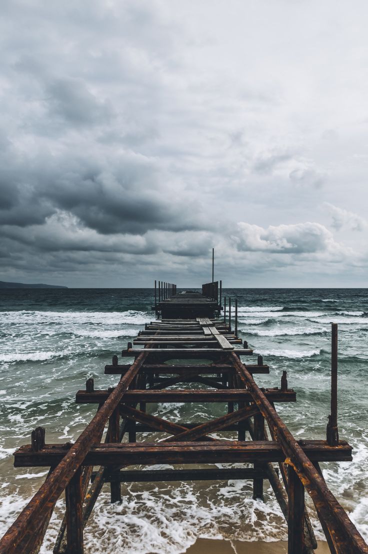 a long wooden pier sitting on top of a sandy beach next to the ocean under a cloudy sky