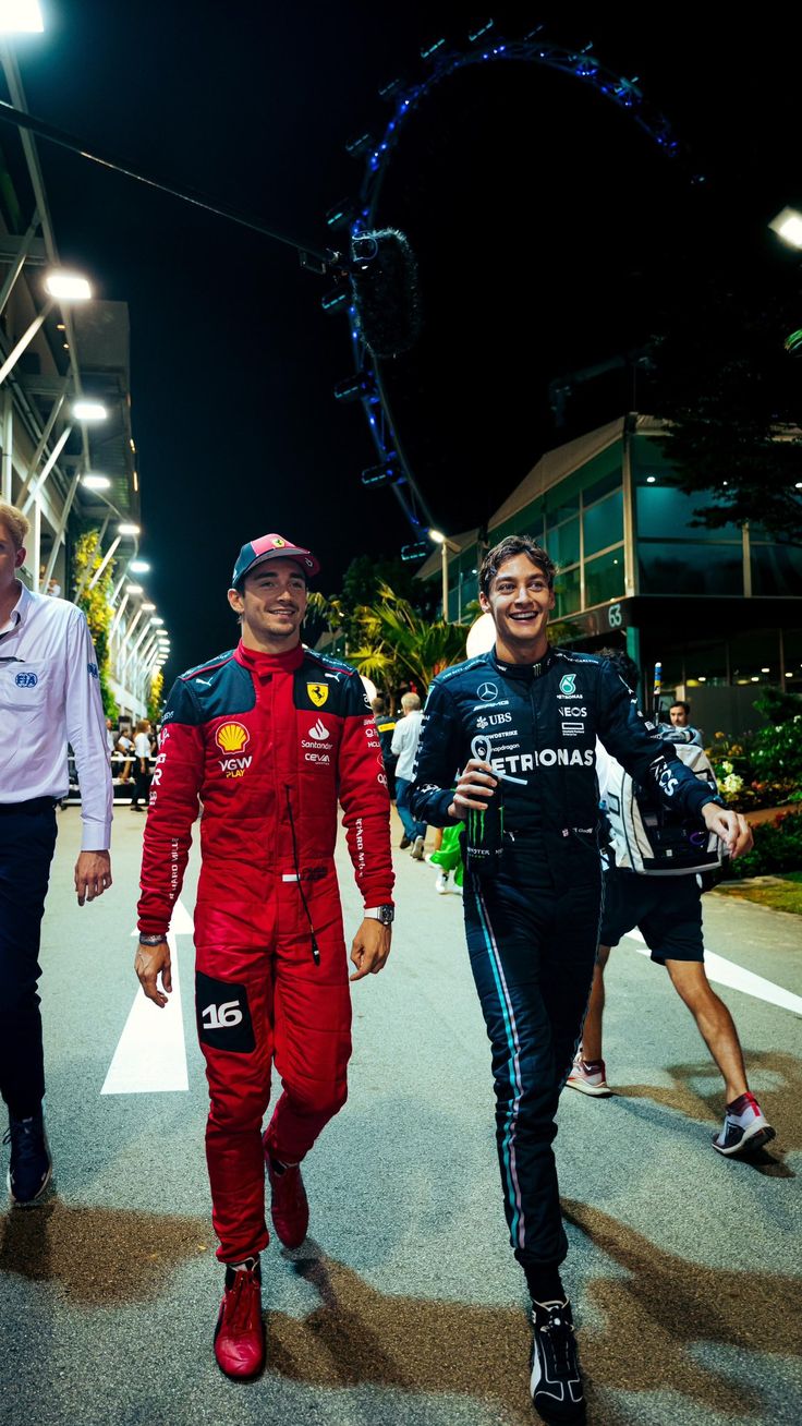 two men are walking down the street at night, one is wearing a racing suit