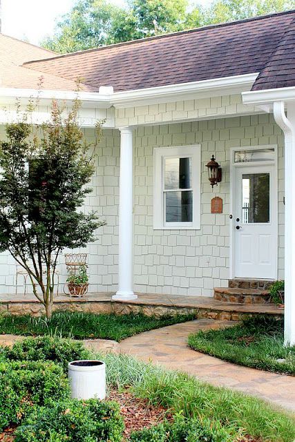 a white house with a tree in the front yard and bushes on the side walk