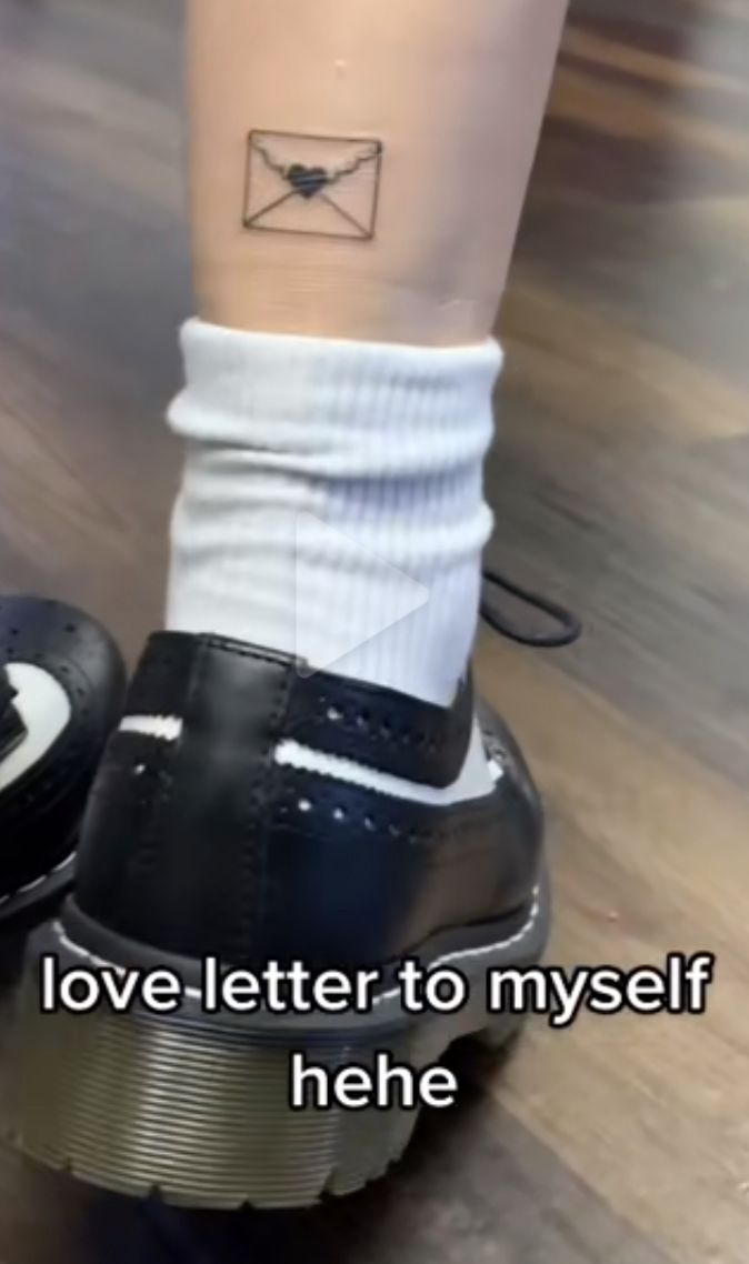 a person with a small tattoo on their leg, standing next to a pair of shoes