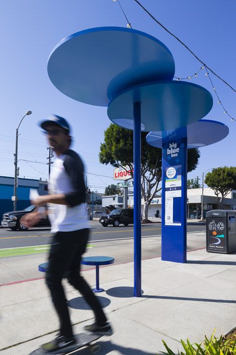 a man riding a skateboard down a sidewalk next to a blue structure with circles on it