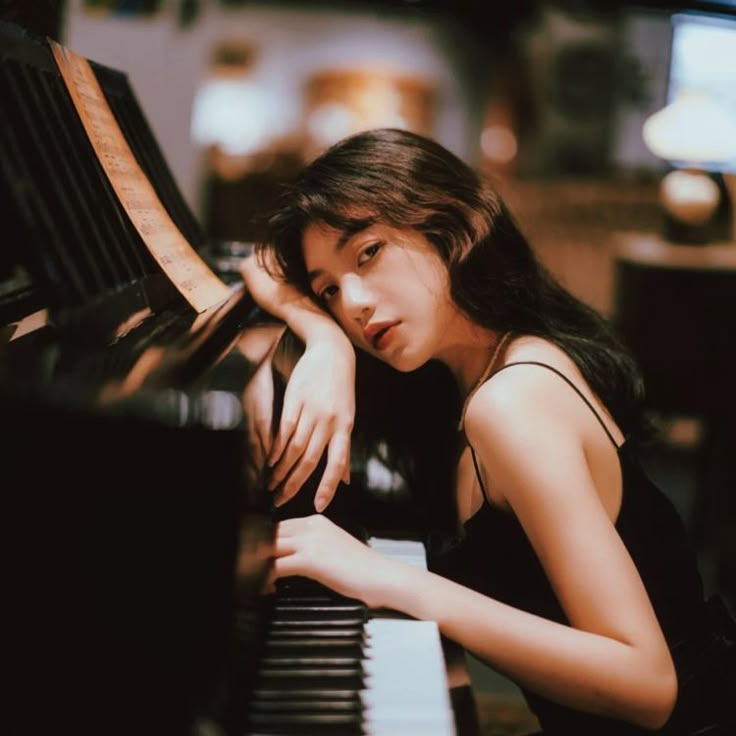 a woman sitting at a piano with her hand on the keyboard and looking down,