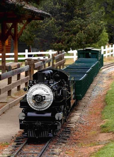 a black train traveling down tracks next to a wooden fence