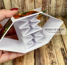 a hand holding an origami bird house made out of folded paper with leaves on it