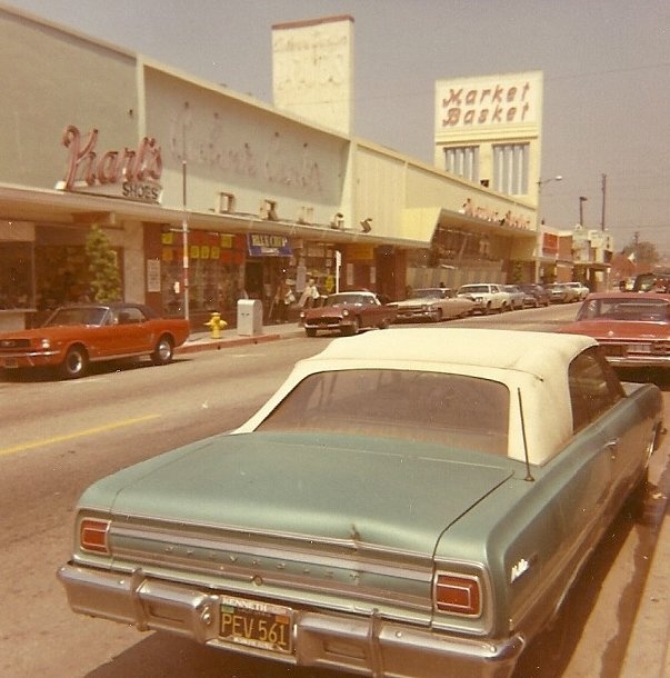 an old car is parked on the side of the road in front of a store