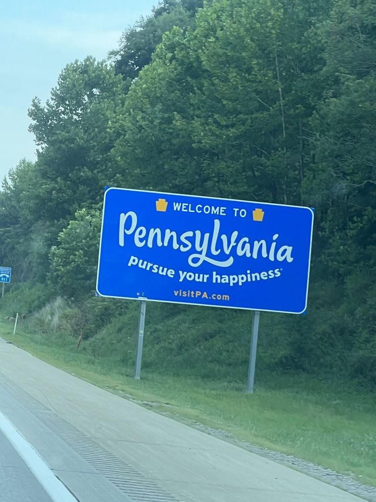 a welcome sign to pennsylvania on the side of a road with trees in the background