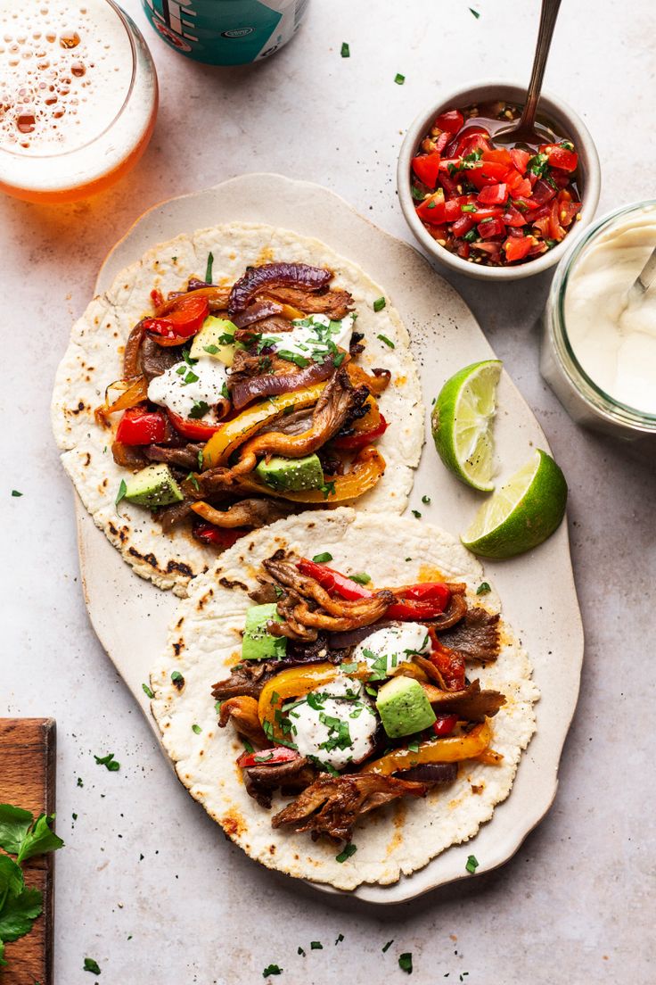 two tortillas with meat, vegetables and sour cream on them next to some condiments