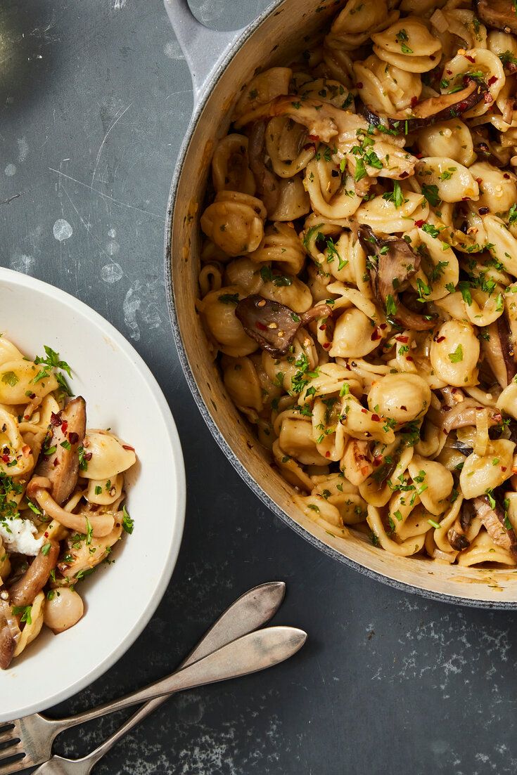 a pan filled with pasta and mushrooms next to a white plate