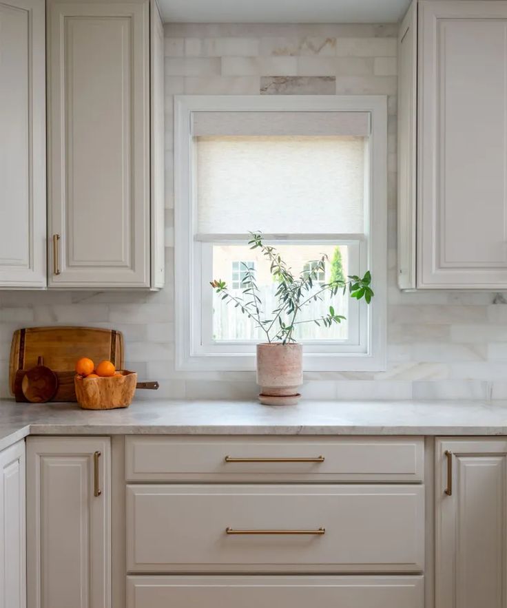 a kitchen with white cabinets and marble counter tops, along with a potted plant on the window sill