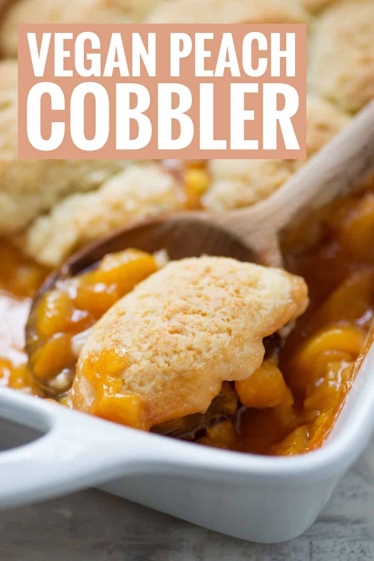 a casserole dish filled with vegan peach cobbler and topped with a wooden spoon