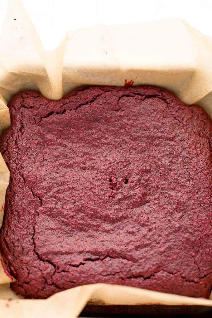 a close up of a red cake in a baking pan with parchment paper on top