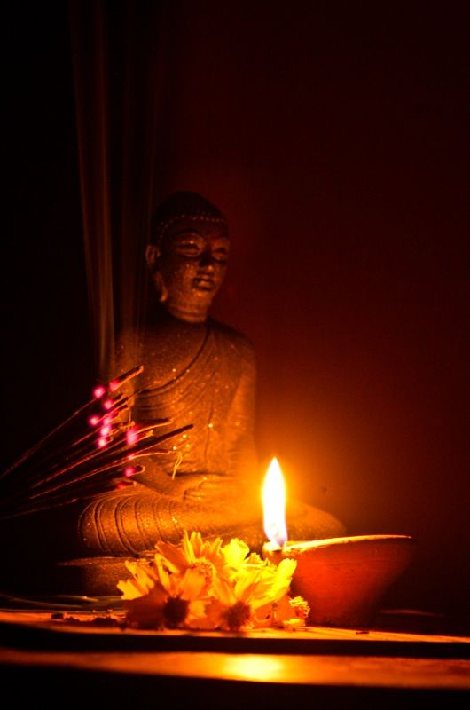 a buddha statue sitting in front of a lit candle