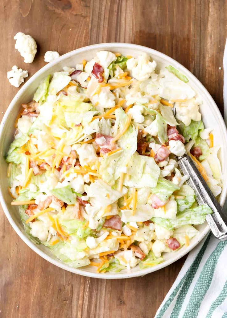 a salad with lettuce, bacon and cheese in a white bowl on a wooden table