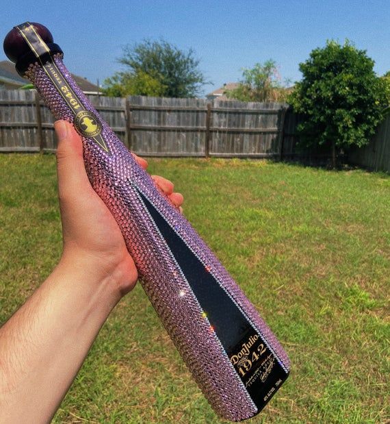 a person holding up a purple bat in their hand with grass and fence behind it