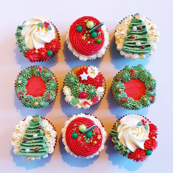 twelve decorated cupcakes arranged in rows on a white surface with green and red decorations