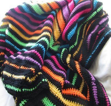 a multicolored crocheted blanket laying on top of a white bed sheet