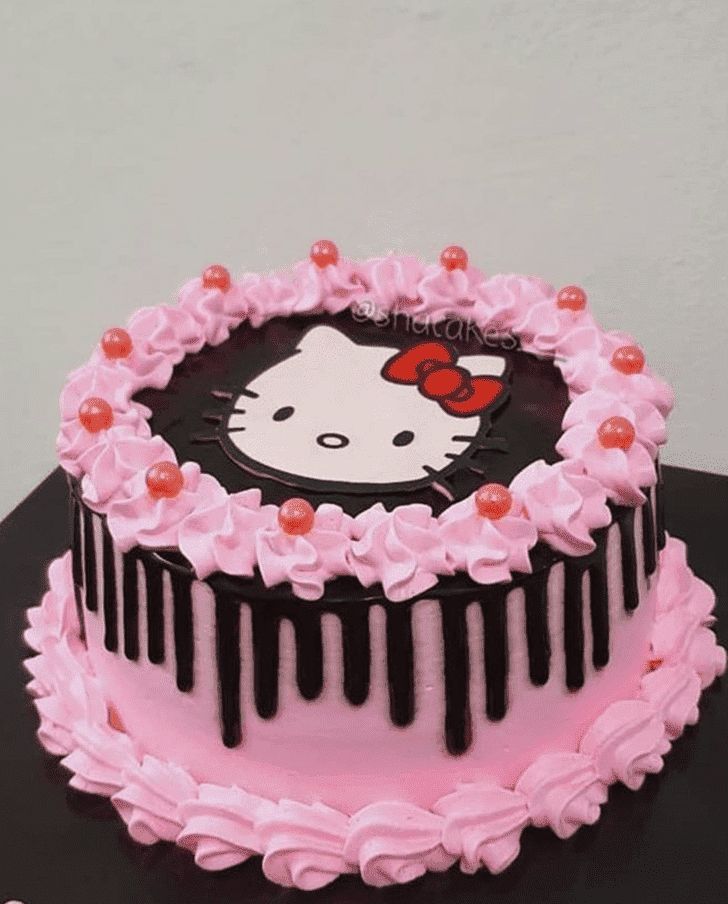 a hello kitty cake with pink icing and chocolate drips on the top, sitting on a table