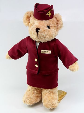 a brown teddy bear wearing a red coat and hat with gold buttons on it's chest