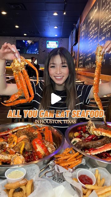 a woman holding up two lobsters in front of some other foods on the table