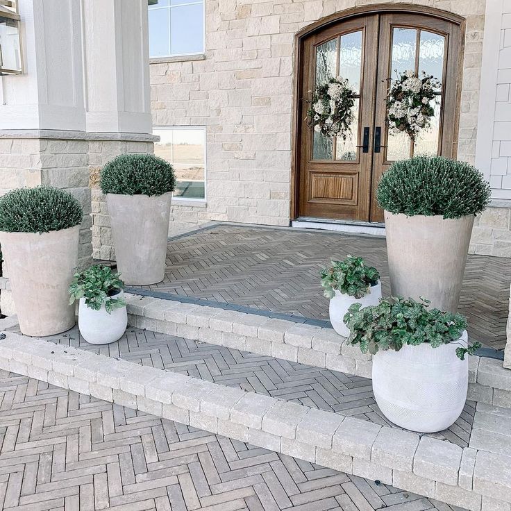 three large white planters sitting on the side of a brick walkway next to a door