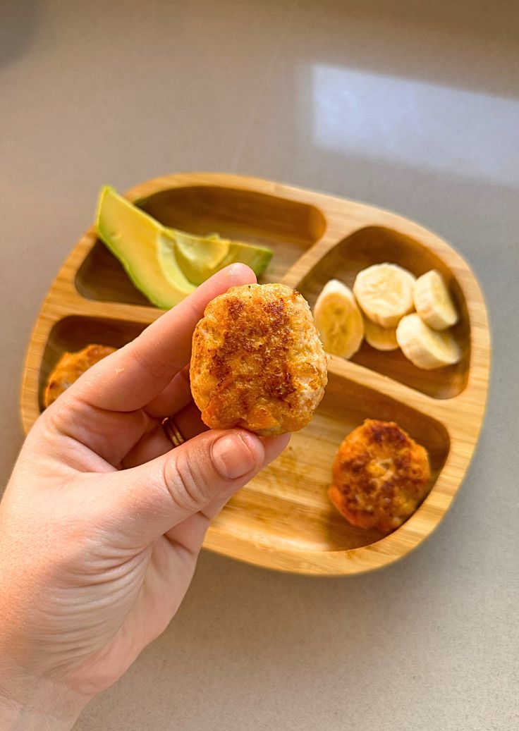 a person is holding food in their hand on a wooden tray with fruit and avocado