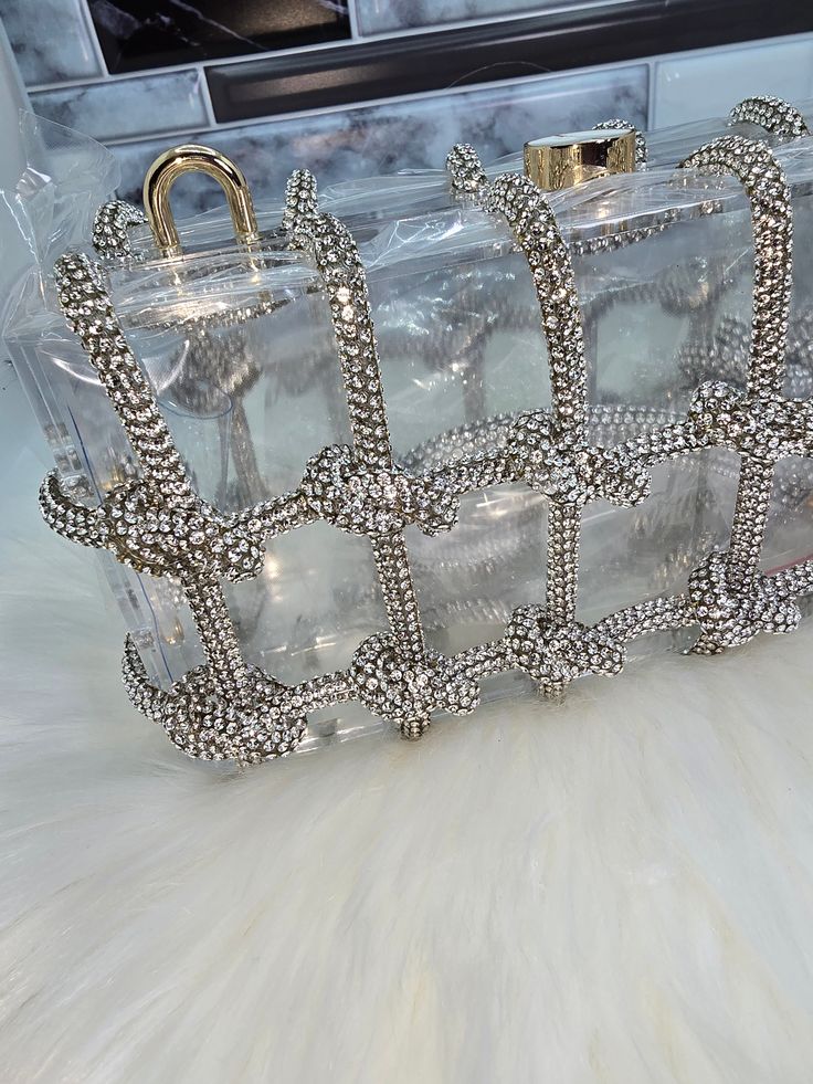 This rhinestone box clutch adds a touch of elegance to your outfit with its clear box design and rhinestone strap. Perfect for a night out or special occasion, it is both stylish and functional. Make a statement with this dazzling accessory! Sparkling Rectangular Clutch For Party, Sparkling Rectangular Clutch For Gift, Elegant Crystal Jewelry For Night Out, Chic Rhinestone Jewelry For Party, Sparkling Rectangular Clutch As Gift, Glamorous Party Clutch With Bling, Trendy Evening Jewelry With Rhinestones, Rectangular Metal Jewelry For Parties, Chic Sparkling Clutch For Party