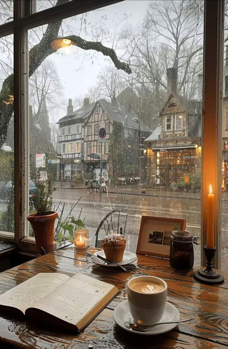 a cup of coffee sitting on top of a wooden table next to a book and candle