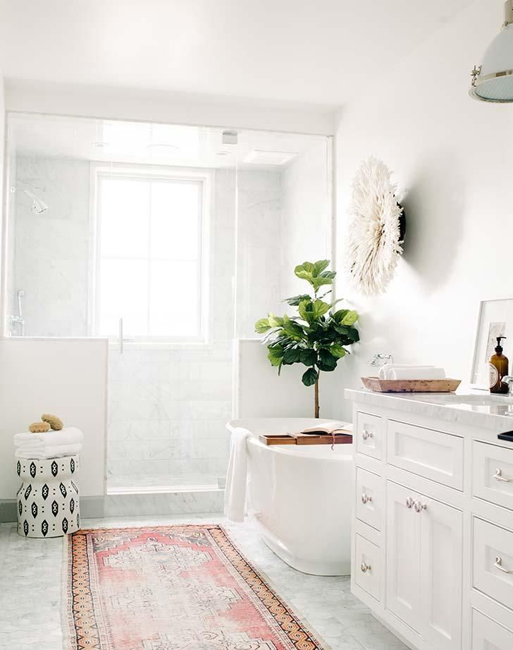 a white bathroom with a rug on the floor and a bathtub next to it