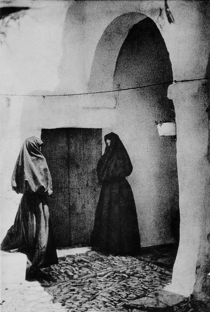 two women in black and white are standing near an open door, one is wearing a veil