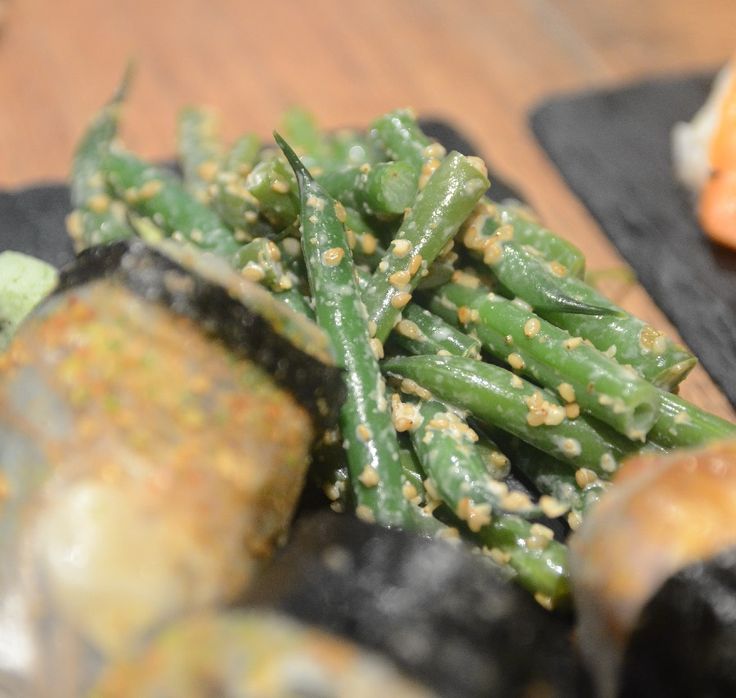 some green beans and other food items on a black plate with chopsticks next to it