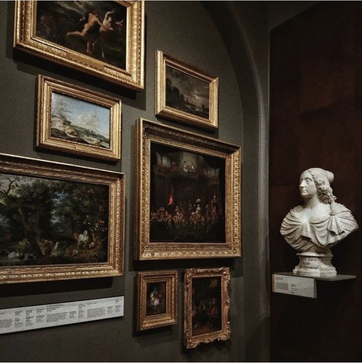 many paintings are on the wall and there is a busturine next to them