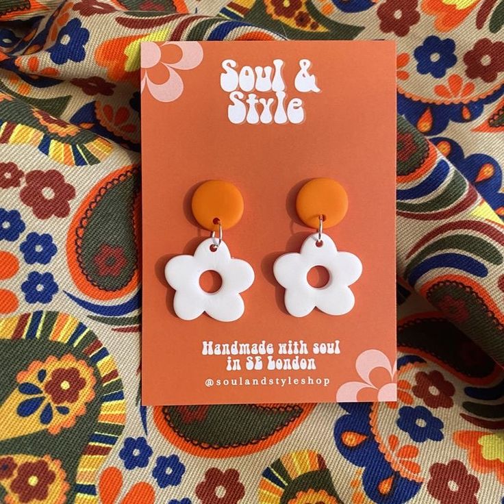 an orange and white pair of earrings sitting on top of a floral print table cloth