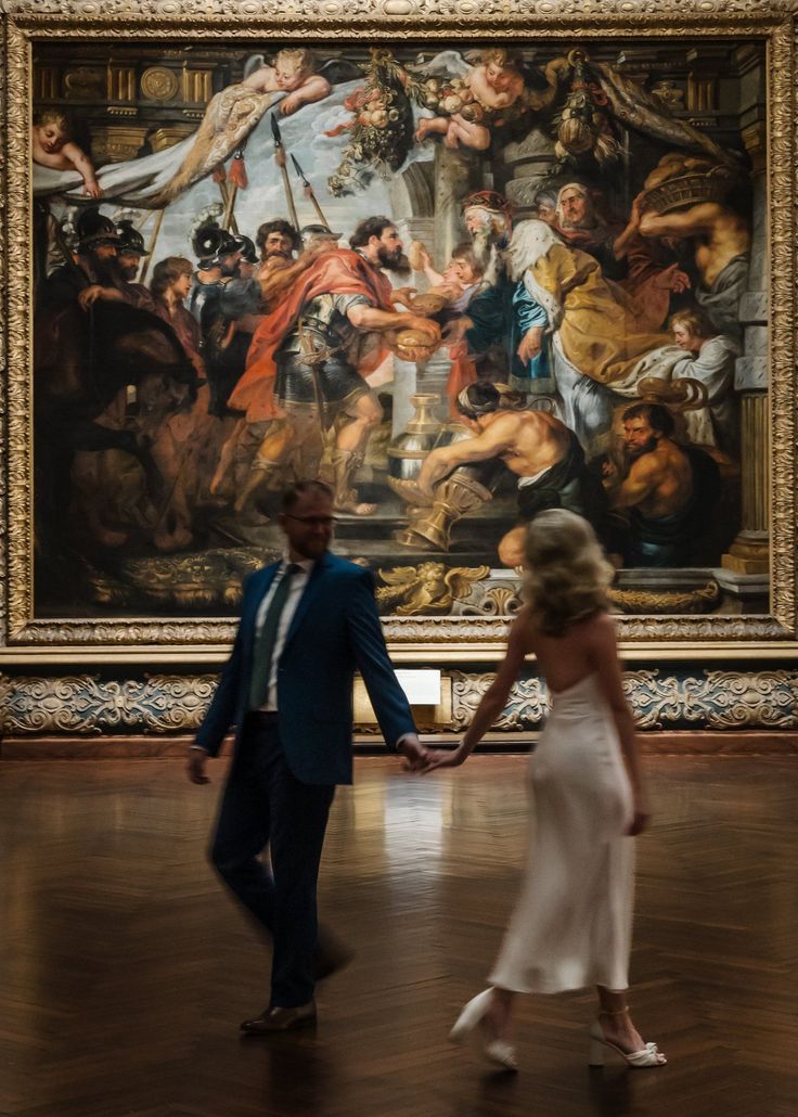 a man and woman holding hands in front of a painting