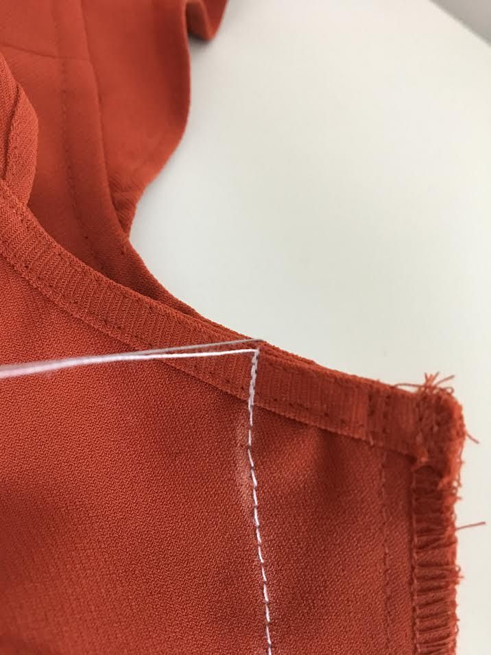 an orange piece of clothing with white stitching on the front and back side, next to a sewing needle