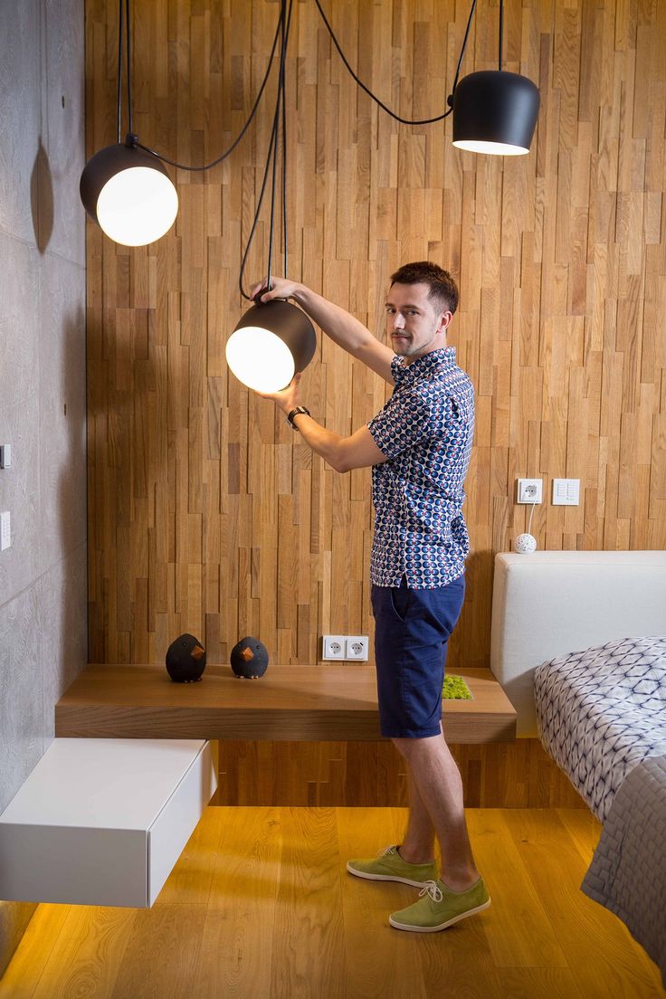 a man standing in front of a wooden wall with three lights hanging from the ceiling