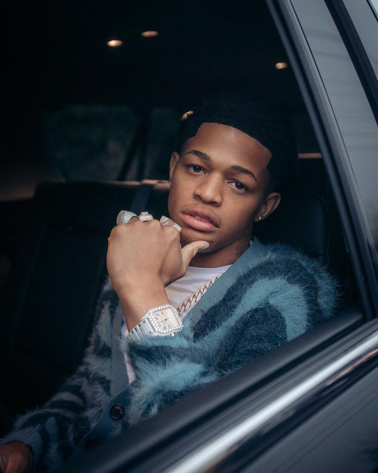 a young man sitting in the back seat of a car wearing a blue and black jacket