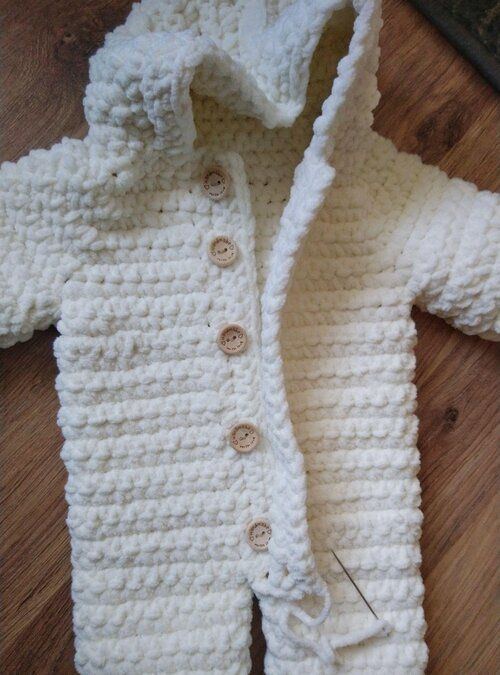 a white crocheted jacket with buttons on the collar and sleeves is laying on a wooden floor