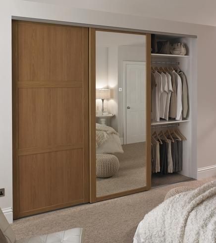 a bedroom with a bed, mirror and closet doors that are open to reveal clothes on hangers