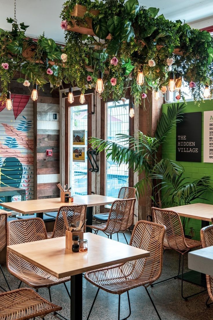 an indoor cafe with plants hanging from the ceiling and wicker chairs in front of them