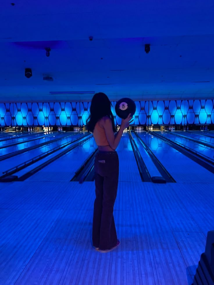 a woman standing in front of a bowling alley holding a disc with lights on it