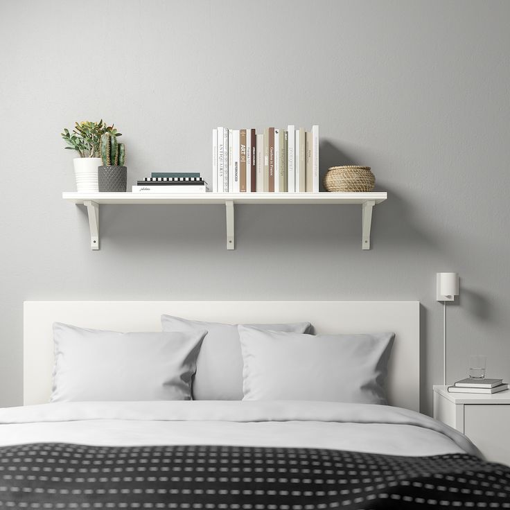 a bed with white sheets and pillows next to a shelf filled with books on top of it