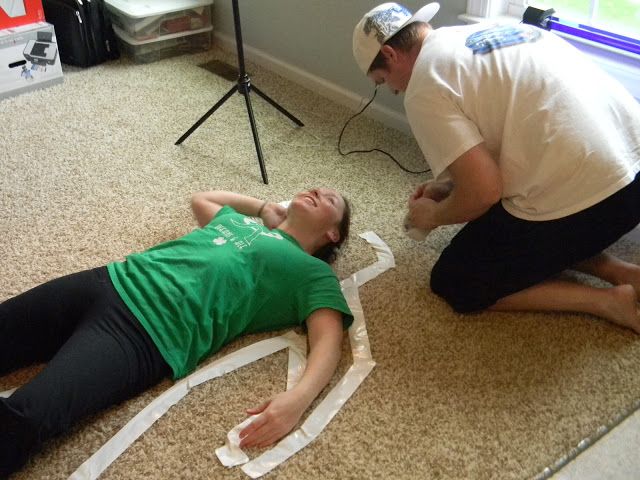 a woman laying on the floor next to a man who is cutting paper with scissors