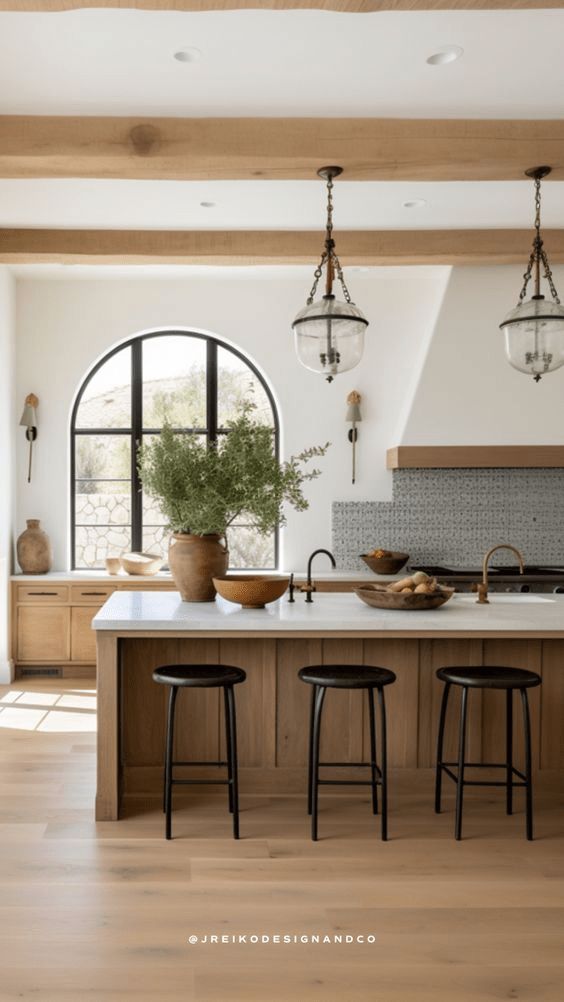 a kitchen with an island and three stools next to the counter top in front of two large windows